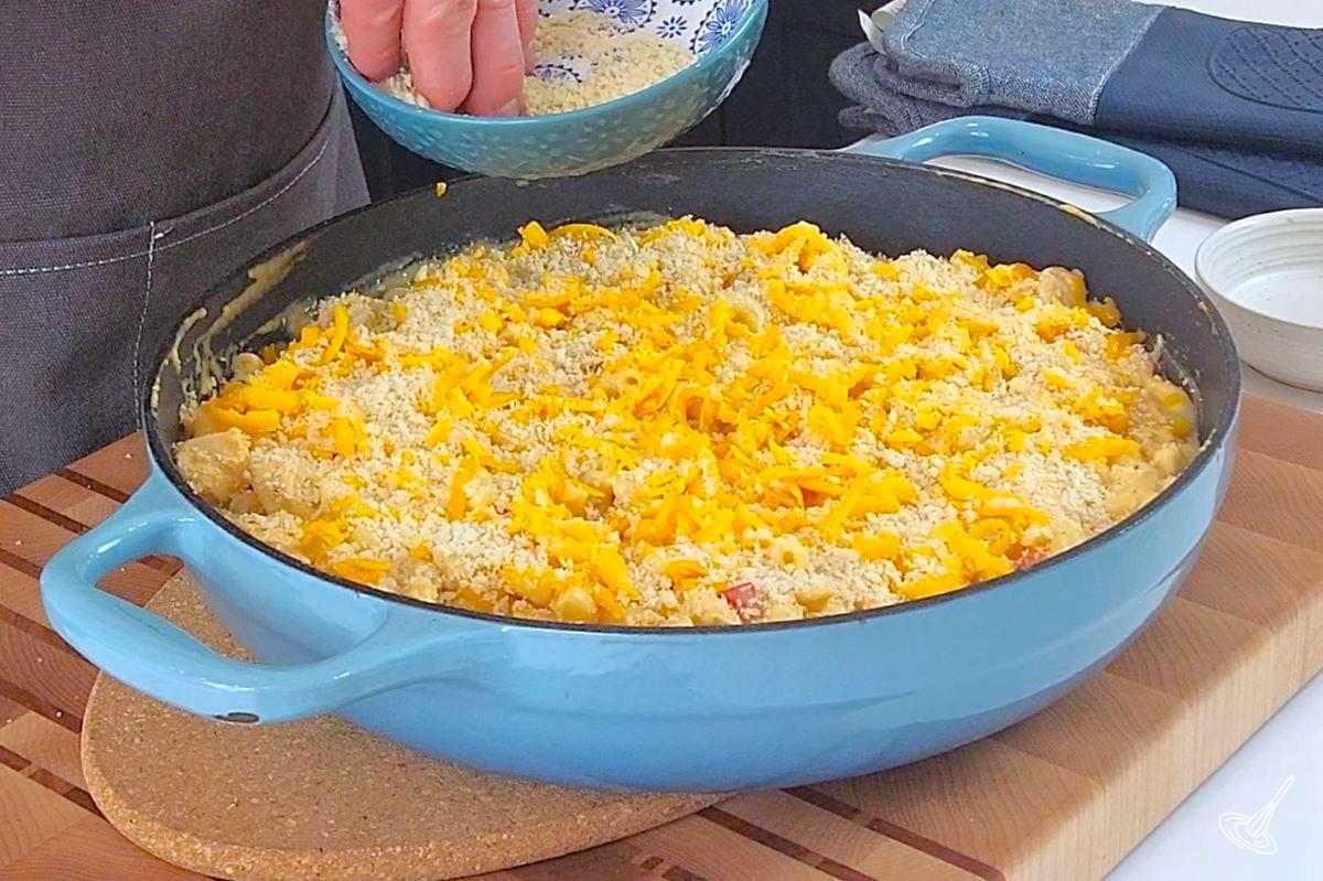 Someone sprinkling panko crumbs on top of a Cajun Chicken Mac and Cheese.