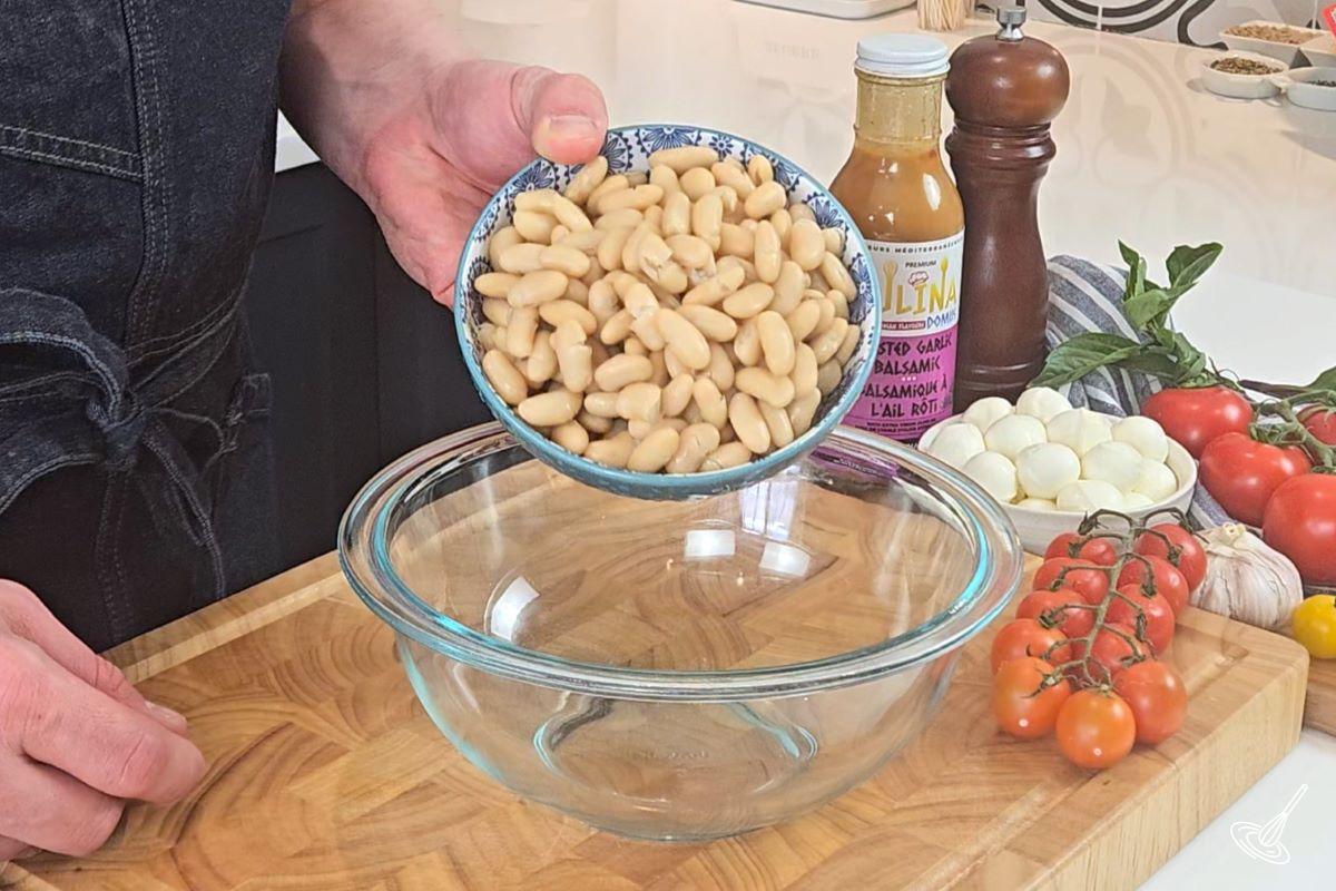 Someone placing white beans into a large bowl.