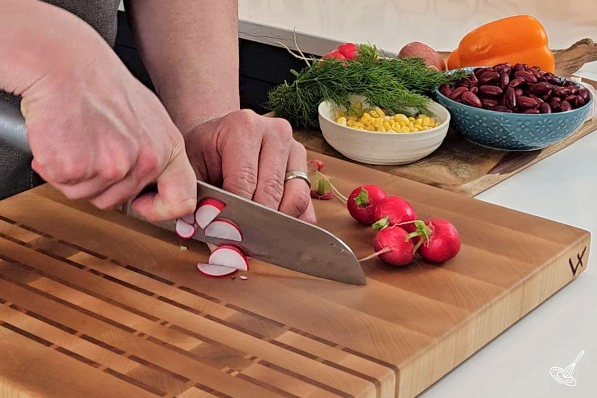 Someone slicing radishes on a wooden cutting board.