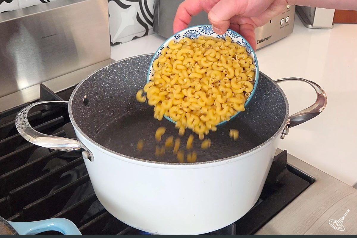 Someone placing elbow macaroni in a large pot of boiling water.