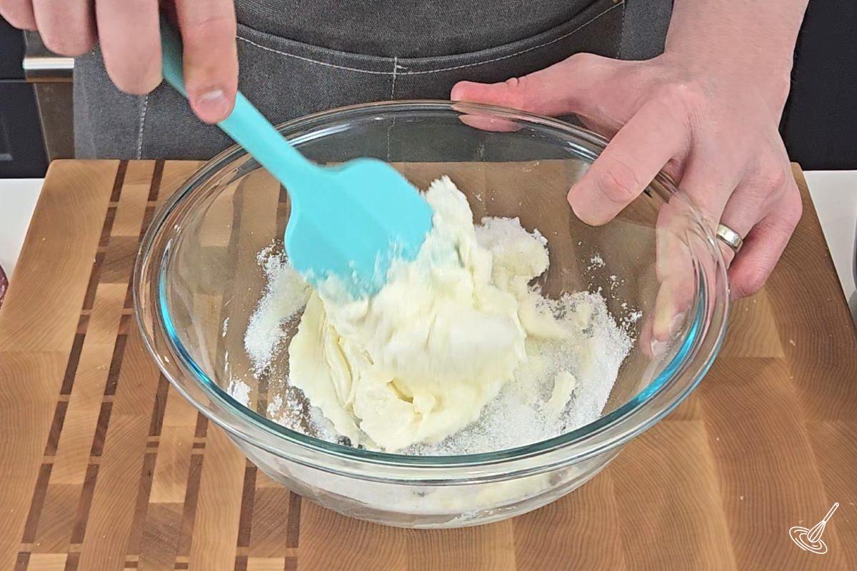 Someone mixing sugar and cream cheese together in a bowl. 