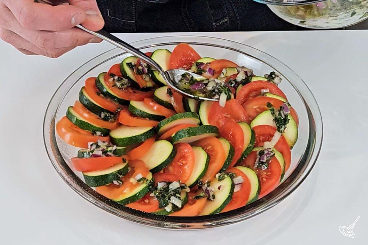 Someone placing an marinade over vegetables in a baking tray.