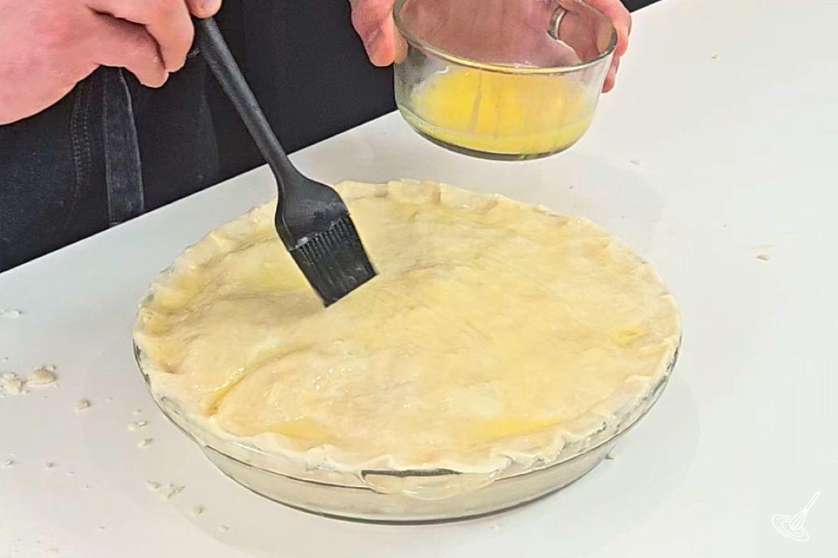 Someone brushing the top of a pie with egg wash. 