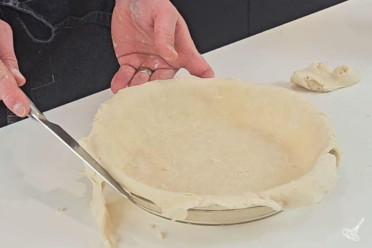 Someone trimming excess dough from the outside of a pie plate.