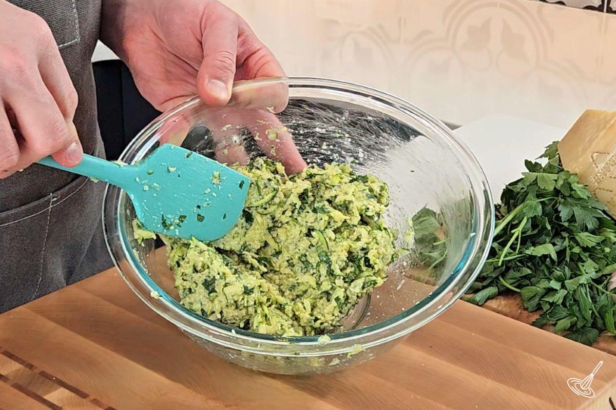 Someone mixing together the batter for zucchini garlic bites in a bowl. 
