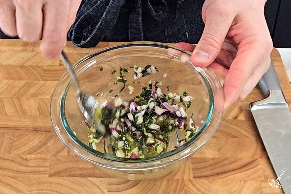 Someone stirring a mixture of olive oil and chopped onions in a bowl.