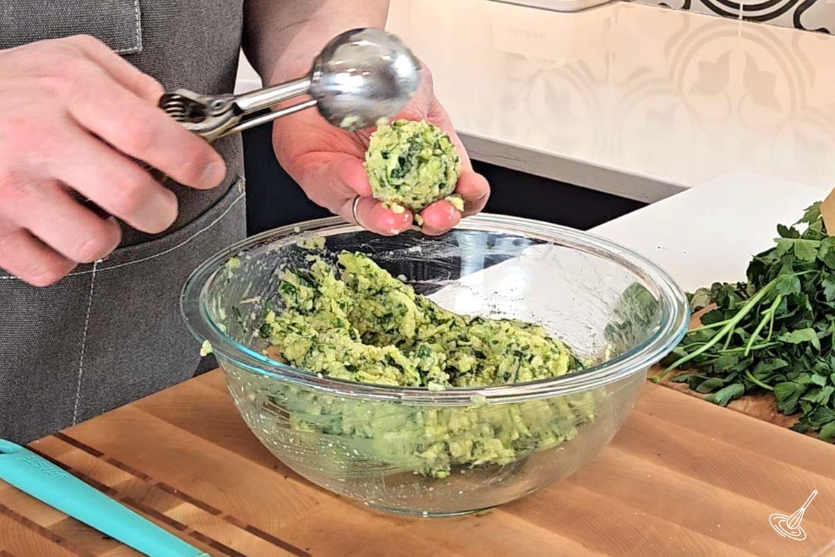 Someone using a cookie scoop to shape the zucchini garlic bites. 