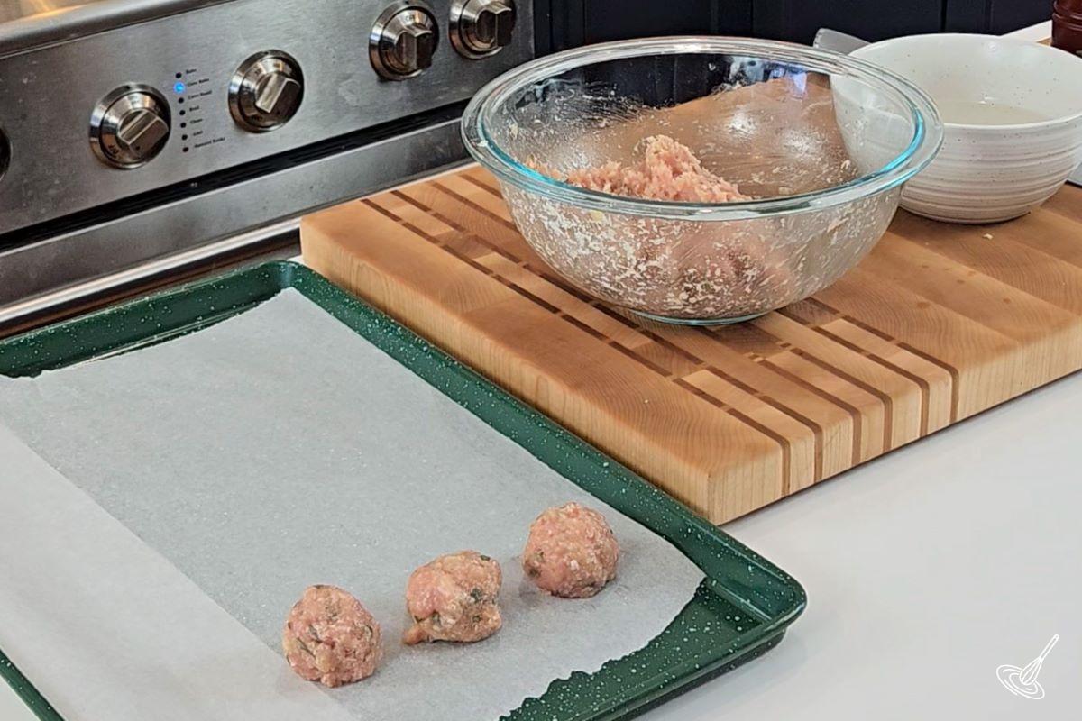 Someone shaping meatballs and placing them on a baking tray. 