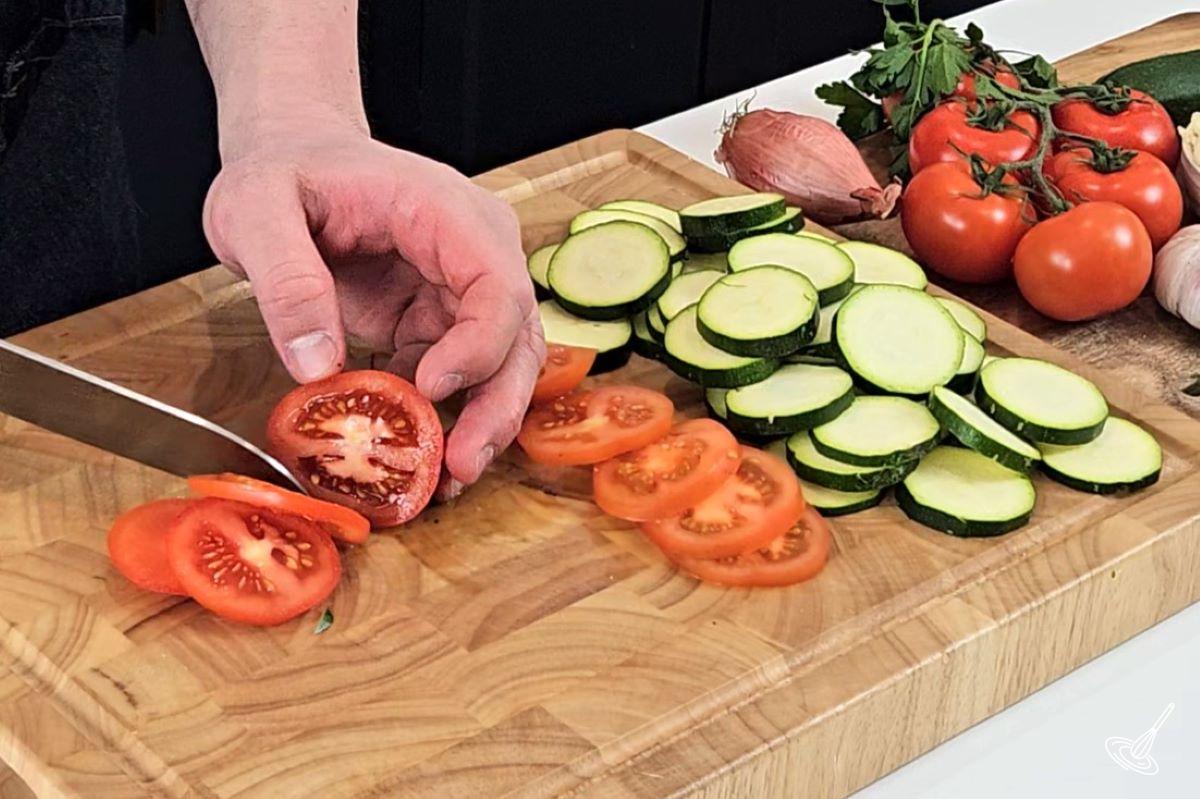 Someone slicing tomatoes on a cutting board.