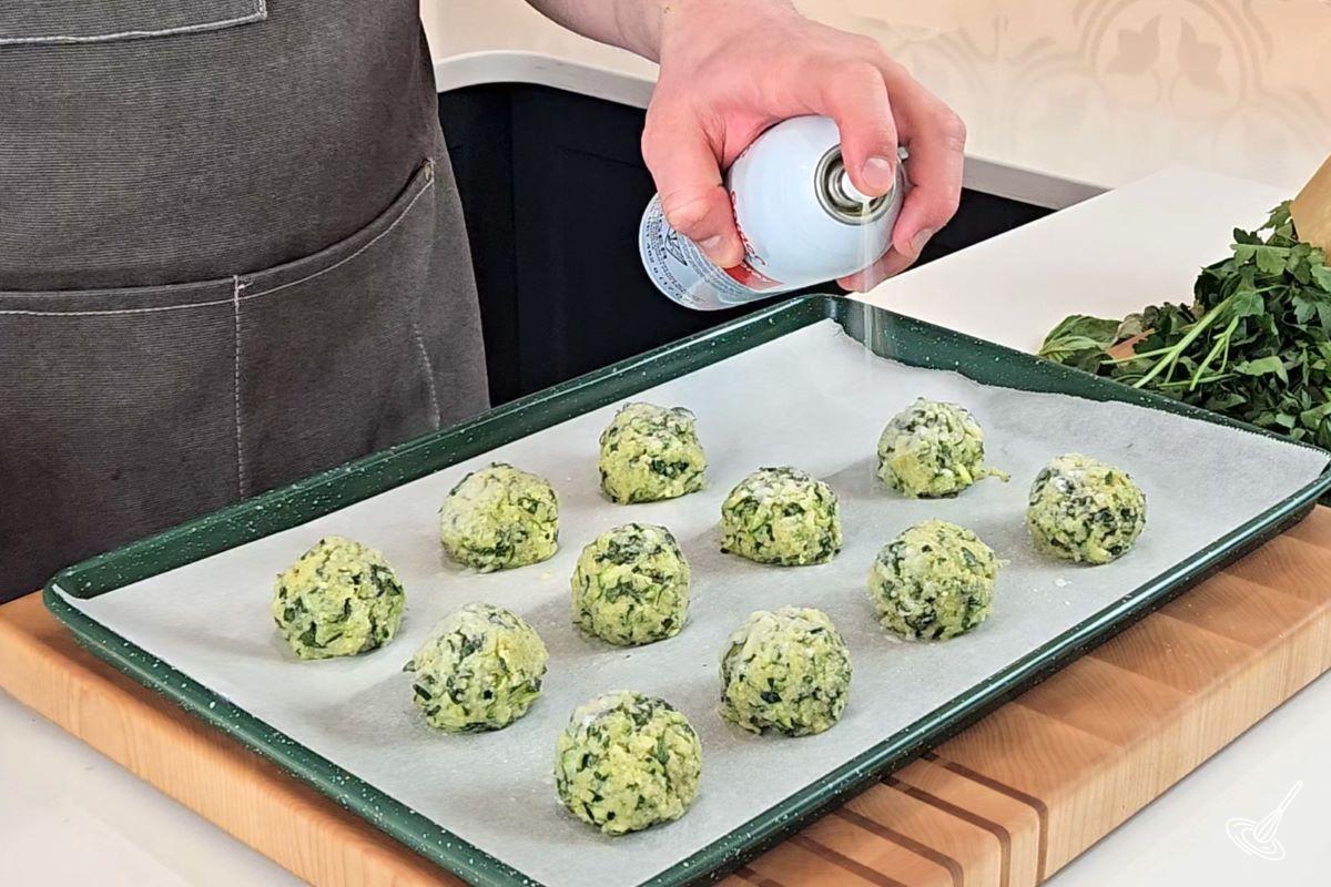 Someone spraying zucchini garlic bites with vegetable spray. 