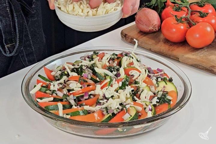 Someone sprinkling cheese over a the caprese zucchini casserole. 