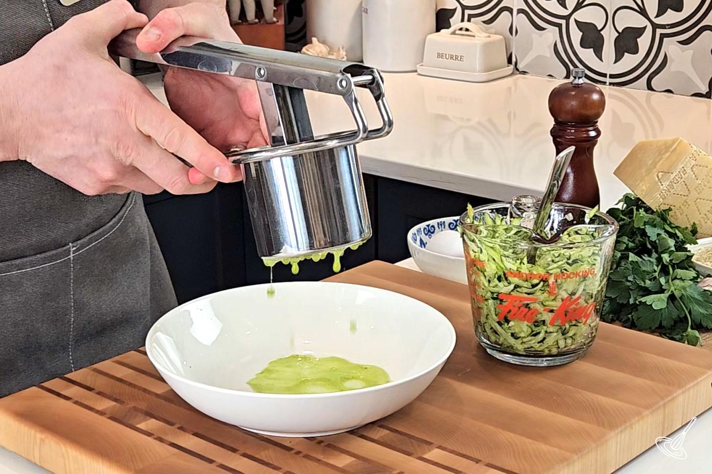 Someone using a potato ricer and squeezing out excess water from grated zucchini. 