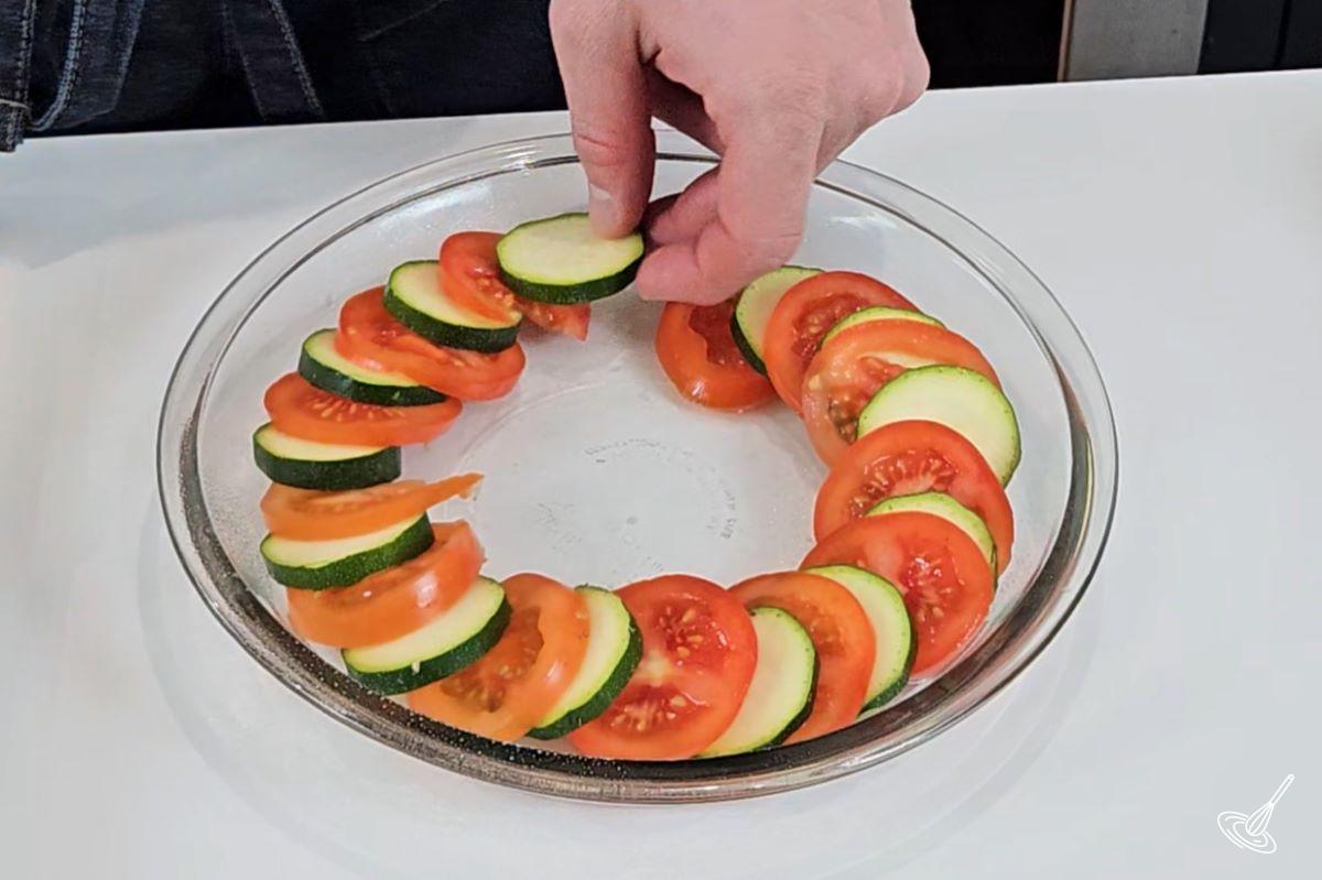 Someone layering slices of zucchini and tomatoes in a baking dish.
