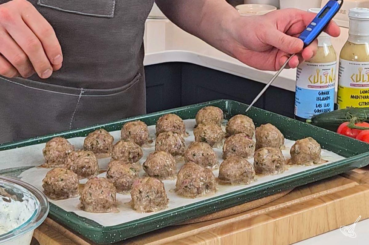 Someone using a probe thermometer on cooked meatballs.
