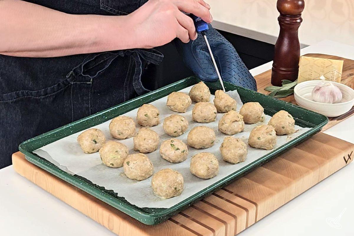 Someone taking the temperature of cooked meatballs with a probe thermometer.
