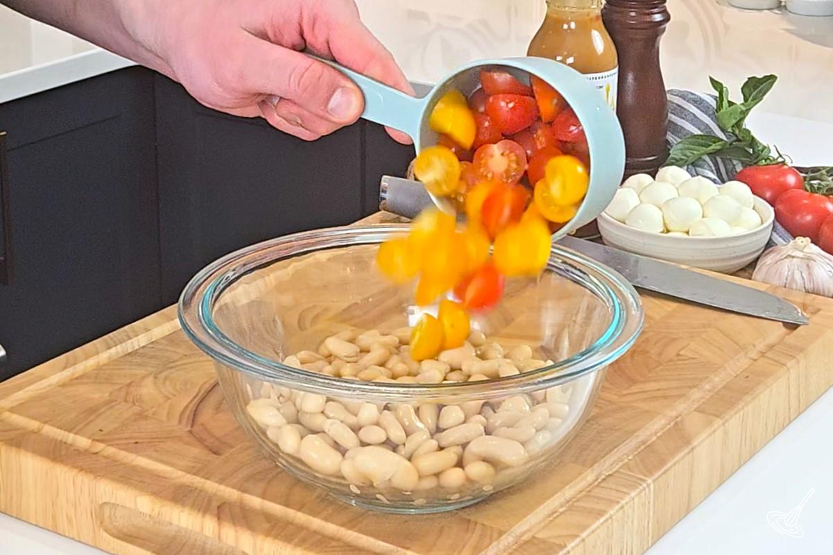 Someone placing tomatoes in a large bowl with white kidney beans. 