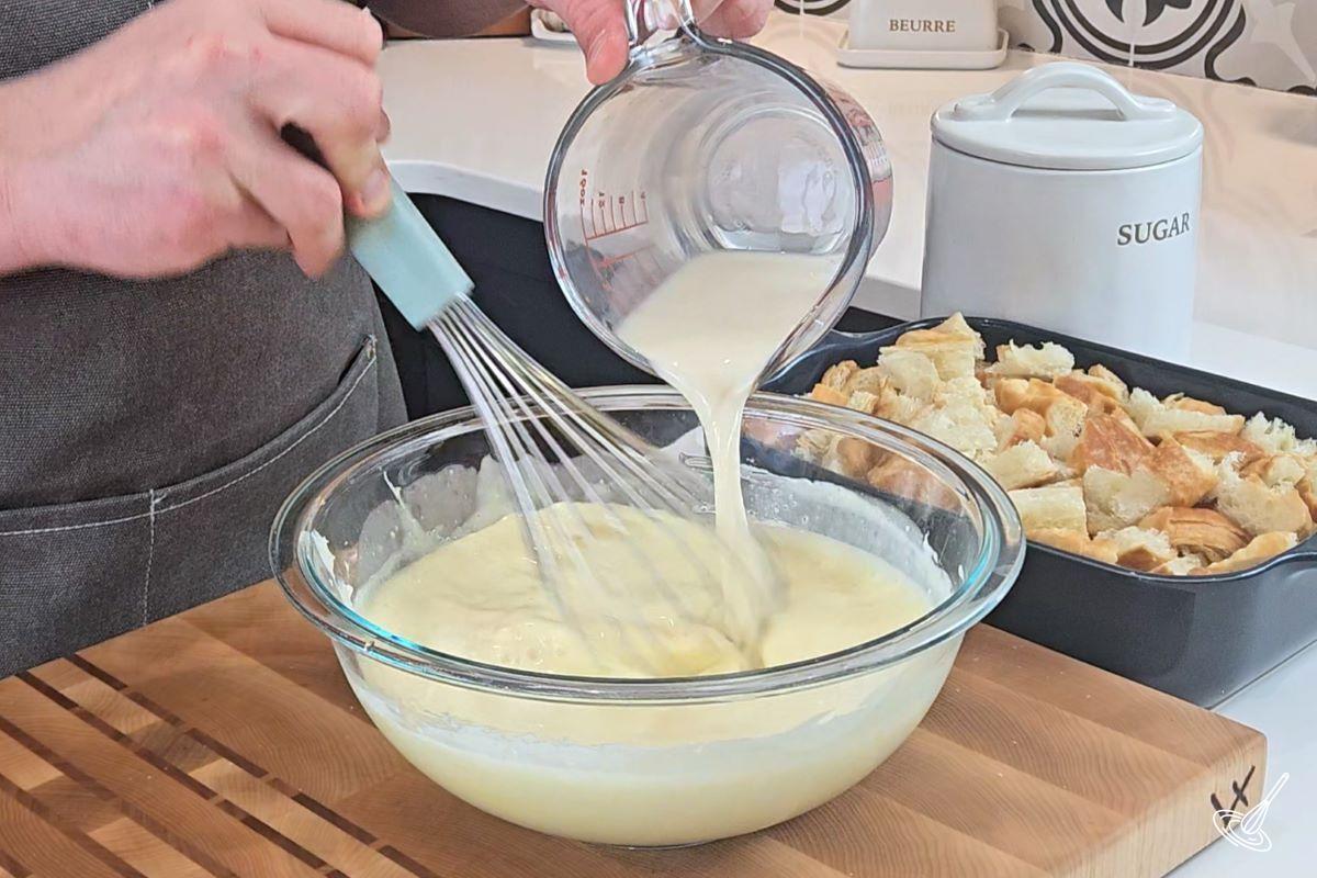 Someone whisking in milk into a bowl of an egg mixture.