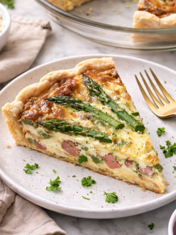 Une part de quiche au jambon et aux asperges dans une assiette.