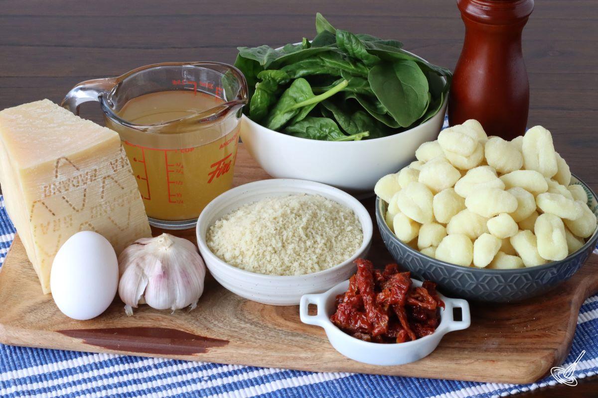 Ingredients on a cutting board including gnocchi, panko crumbs, parmesan, sundried tomatoes and fresh spinach. 