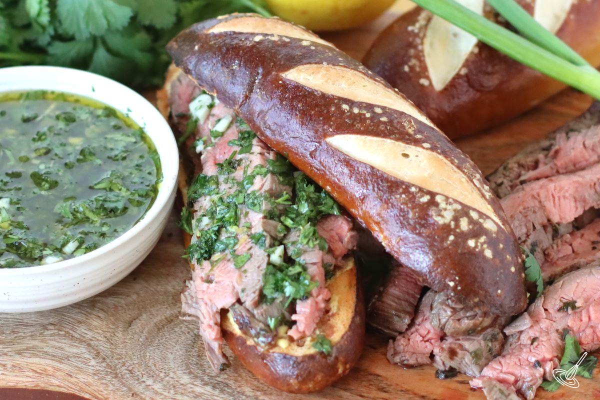 A Chimichurri Steak Sandwich on a cutting board with a side of chimichurri sauce.