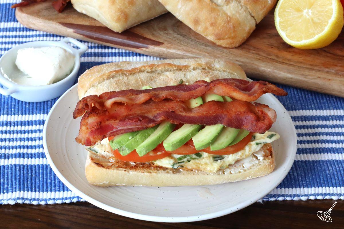 A Ciabatta Breakfast Sandwich being built on a plate. 