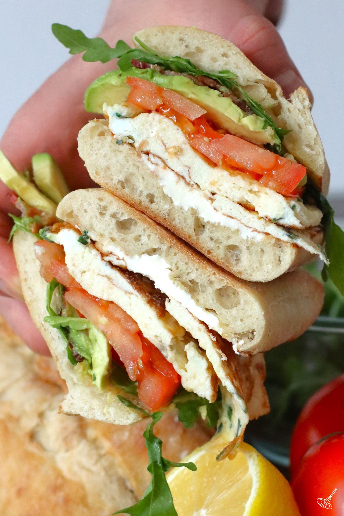 Someone holding a Ciabatta Breakfast Sandwich cut in half.