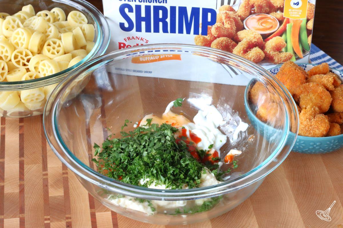 A glass bowl containing mayonnaise, Greek yogurt, and fresh herbs.