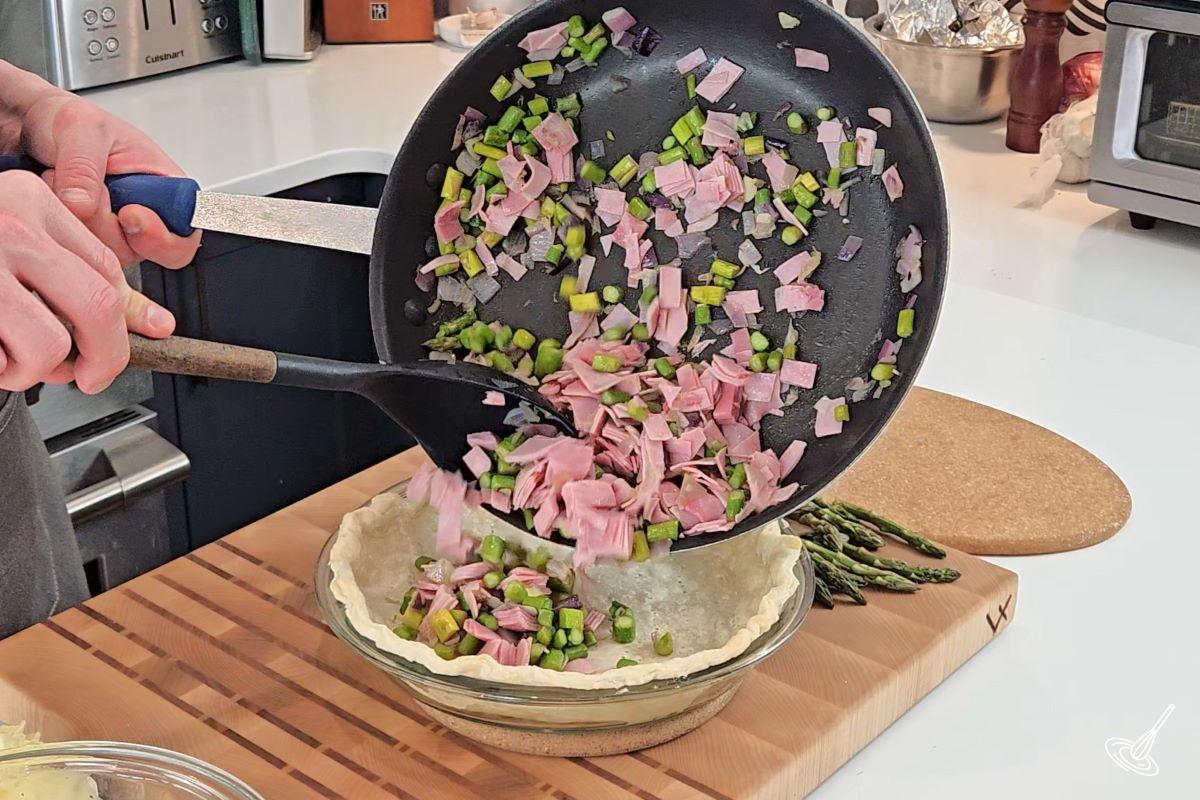 Quelqu'un verse un mélange de jambon et de légumes dans une pâte à tarte.