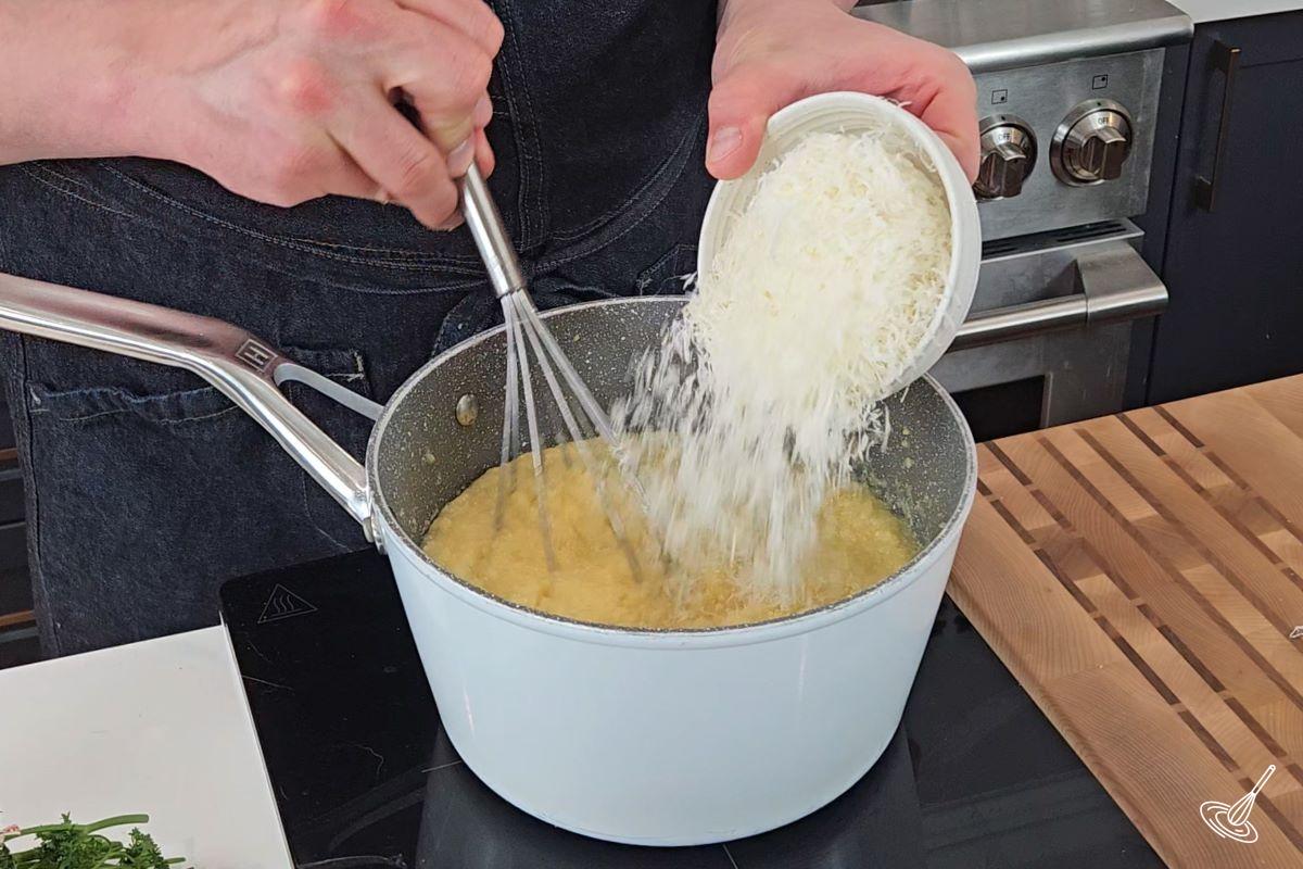 Someone adding grated parmesan into a saucepan with creamy polenta.