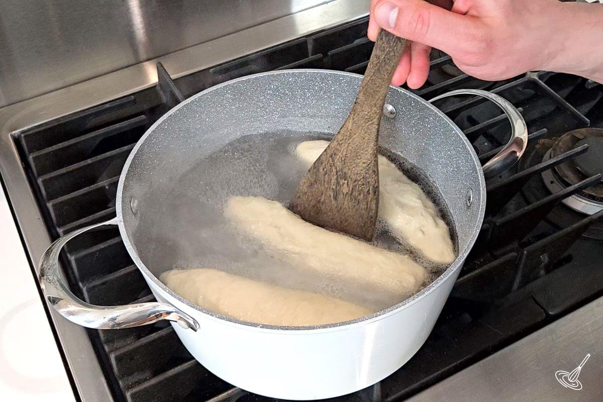 Someone using a wooden spatula to flip over a bun in a pot of water.