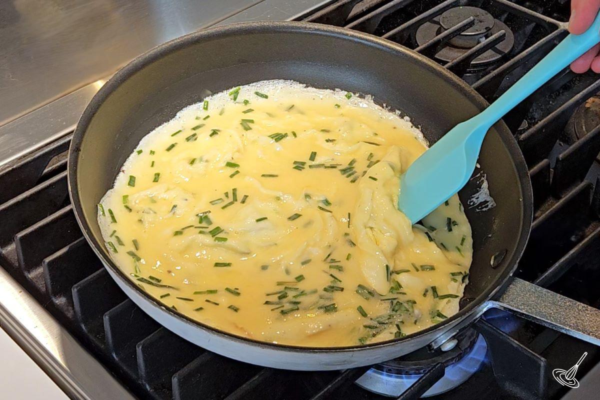 Someone stirring scrambled eggs in a large frying pan. 