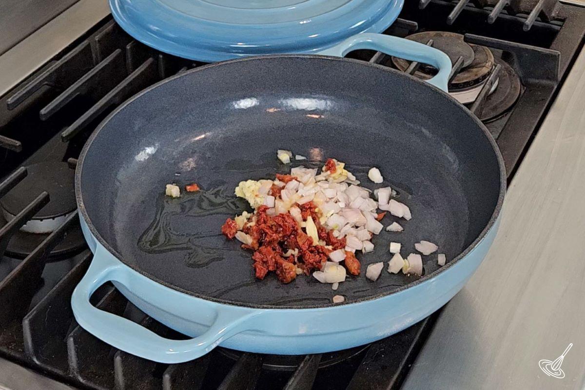 A large skillet on the stove, containing shallot and sundried tomatoes.