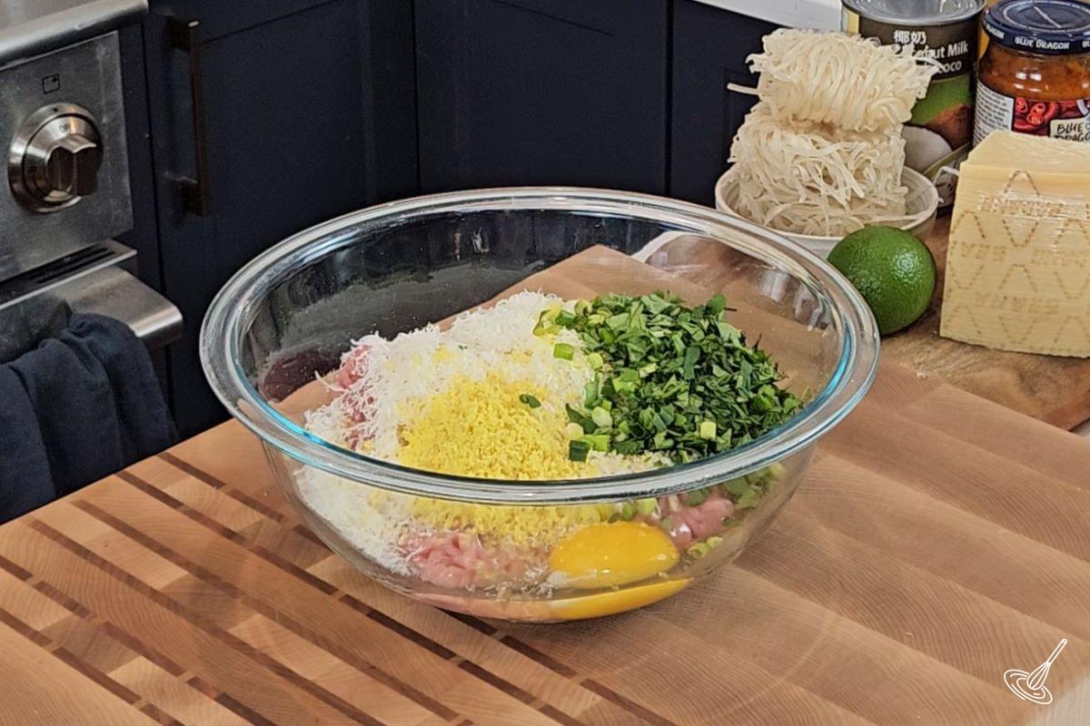 Ground chicken in a large bowl with grated ginger, herbs, panko crumbs, and grated parmesan. 
