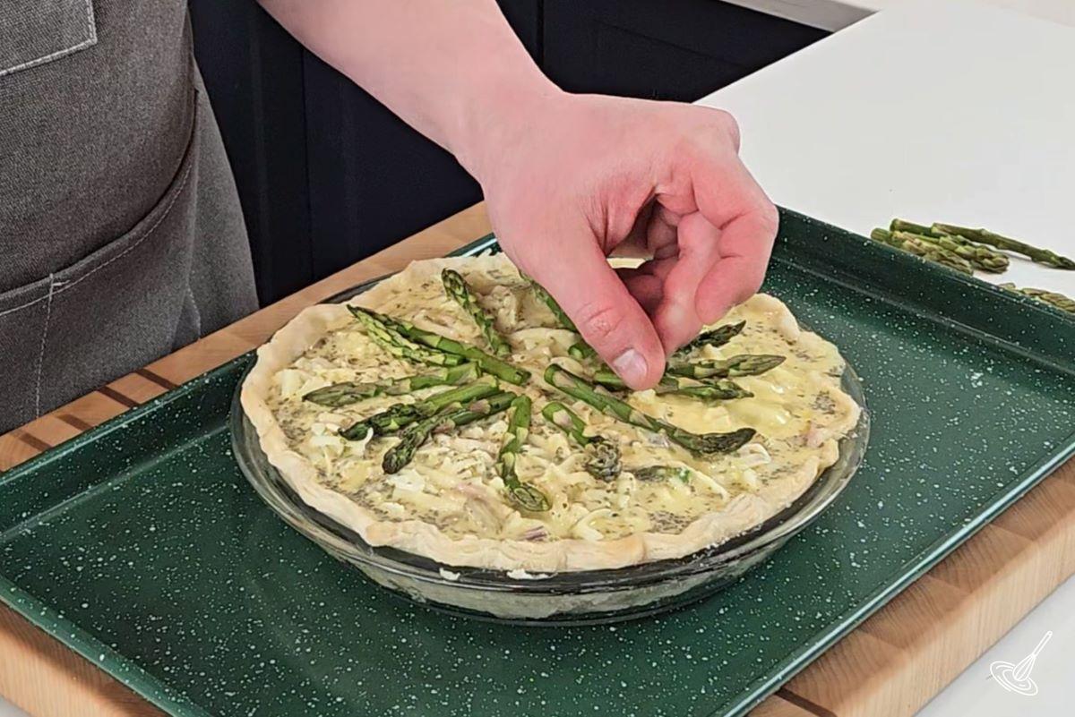 Quelqu'un qui dépose des fanes d'asperges sur une quiche avant de la cuire. 