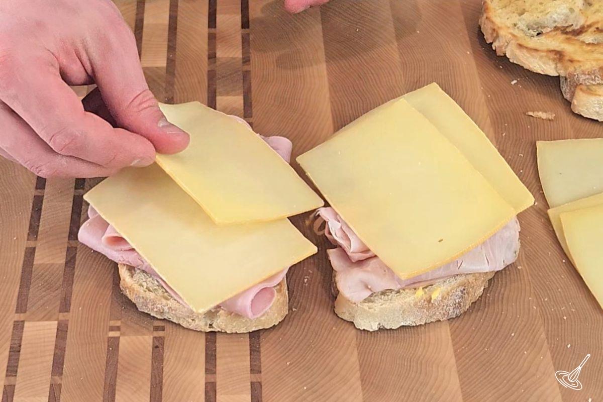 Someone placing slices of raclette cheese on a sandwich.