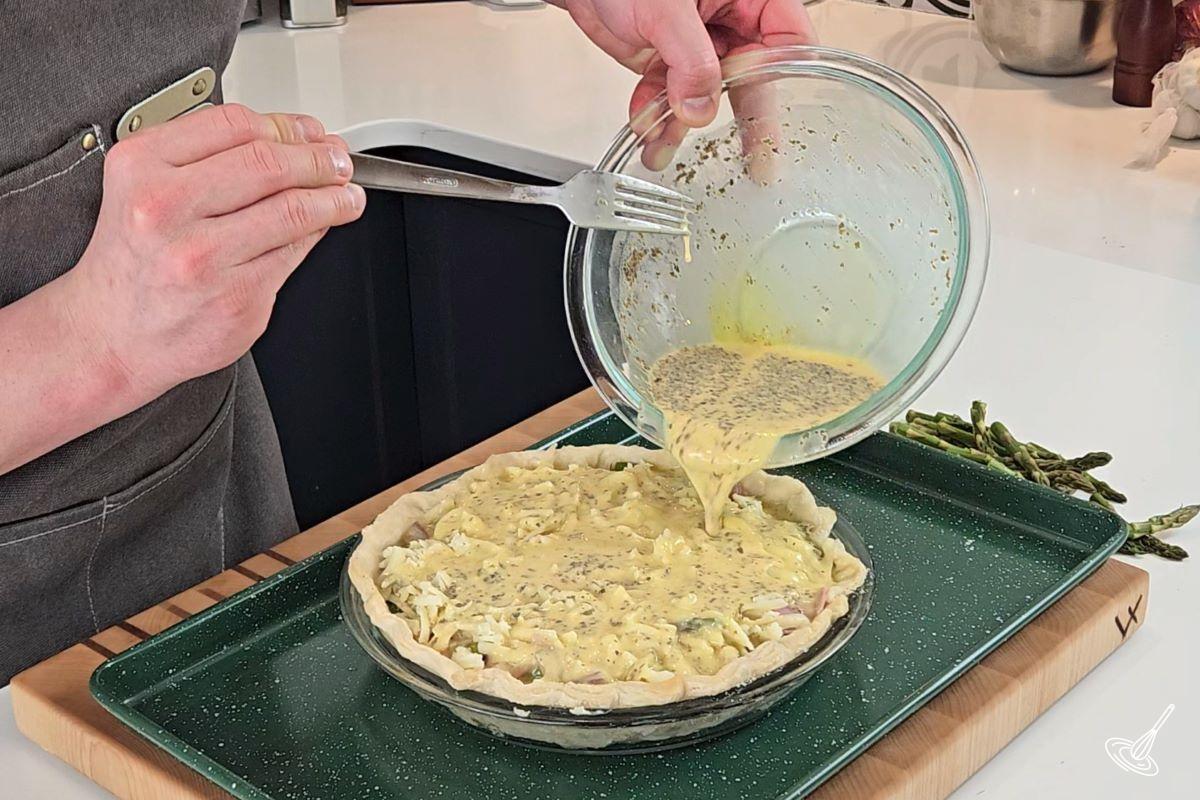 Quelqu'un verse un mélange d'œufs et de lait sur une quiche.