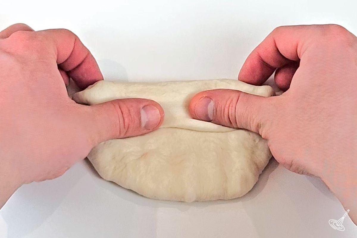 Someone using their thumbs and indexes to shape a piece of dough. 