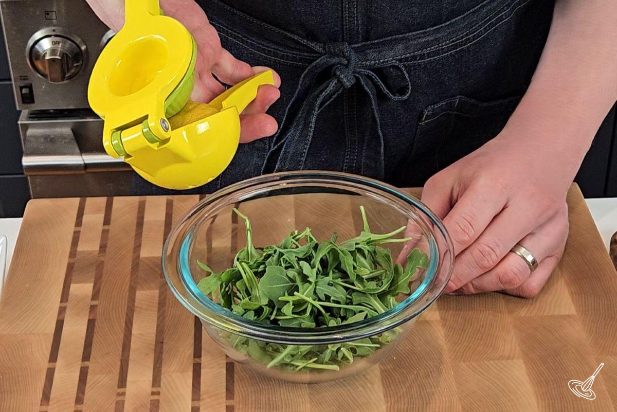 Someone squeezing fresh lemon juice in a small bowl of arugula. 