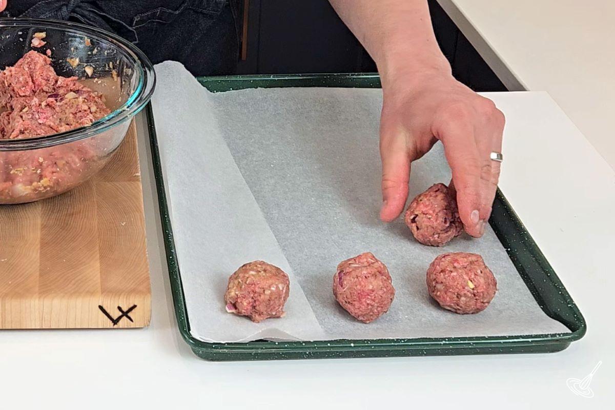 Someone placing a meatball on a parchment paper lined baking tray.