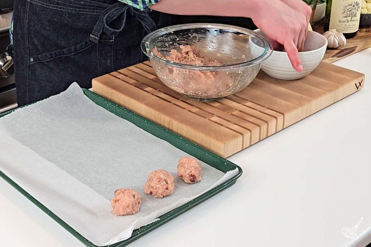Someone shaping meatballs and placing them on a baking tray.