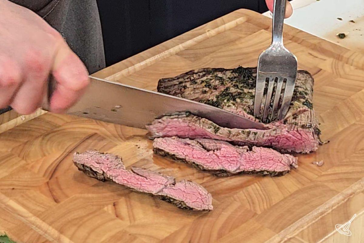 Someone slicing a steak on a wooden cutting board.