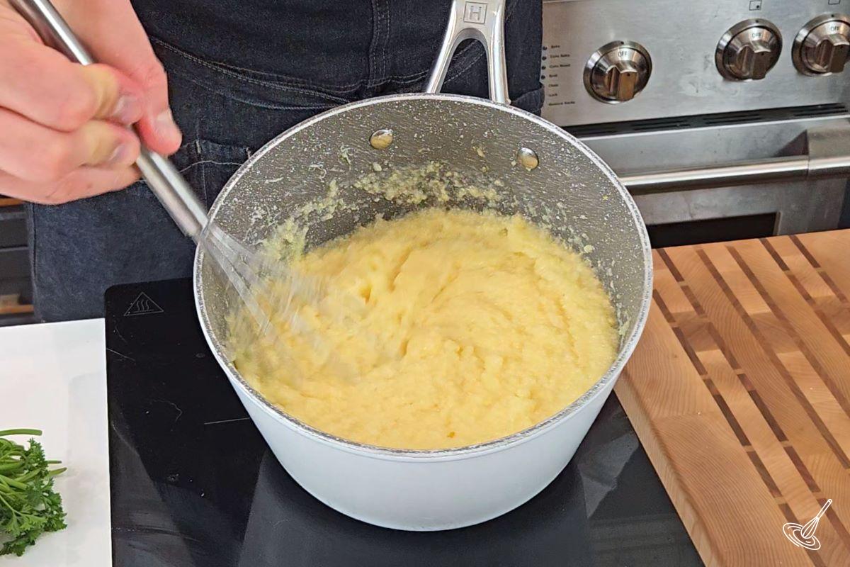 Someone whisking creamy polenta in a saucepan. 