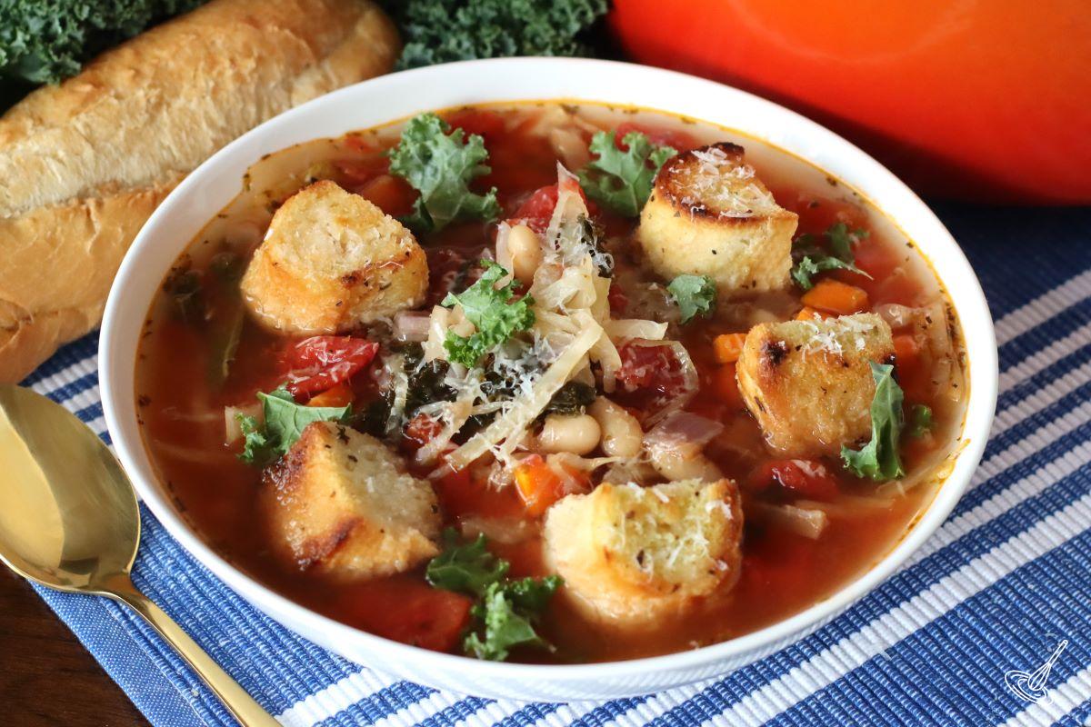 Cabbage and Kale soup in a bowl, garnished with croutons and parmesan cheese.