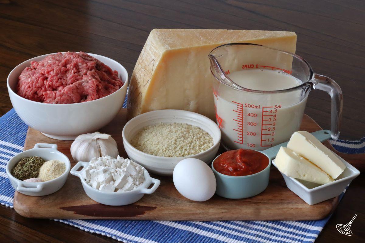 Ingredients on a wooden board, including ground beef, panko crumbs, milk, butter, flour, and spices.