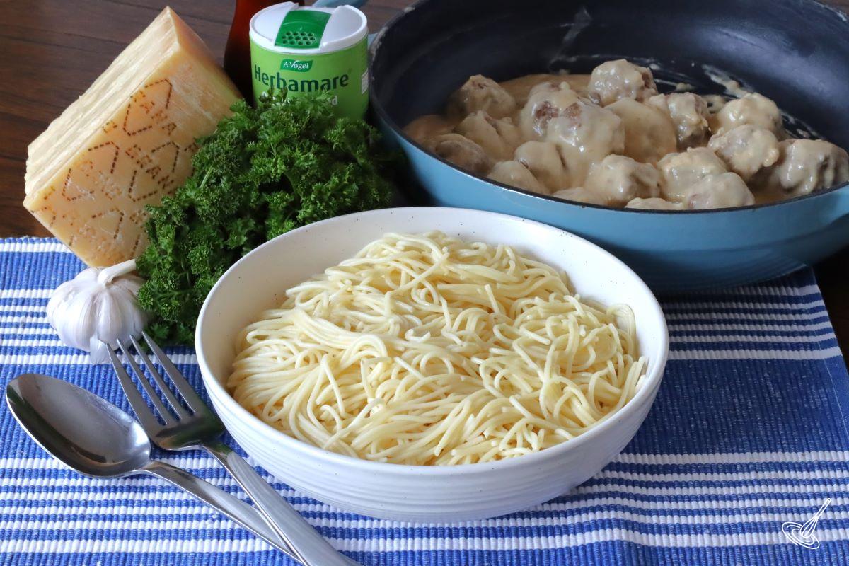 A large bowl of spaghetti on a table with a skillet of Alfredo Meatballs behind it. 