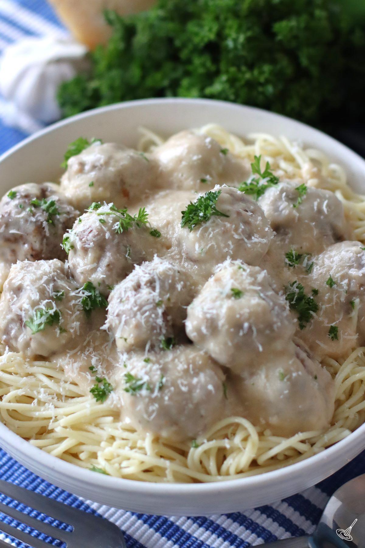 Alfredo Meatballs on top of spaghetti in a serving bowl.