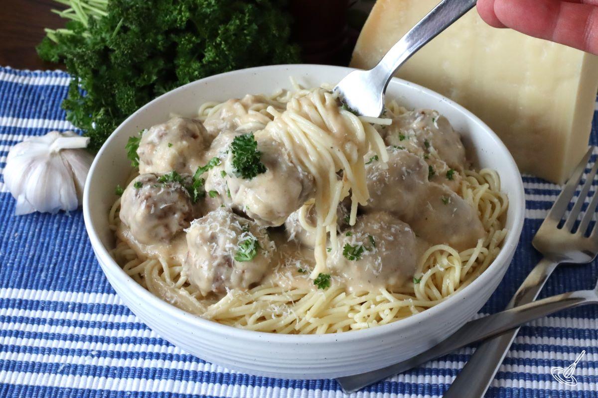 Someone holding up a fork with Alfredo Meatballs with spaghetti.