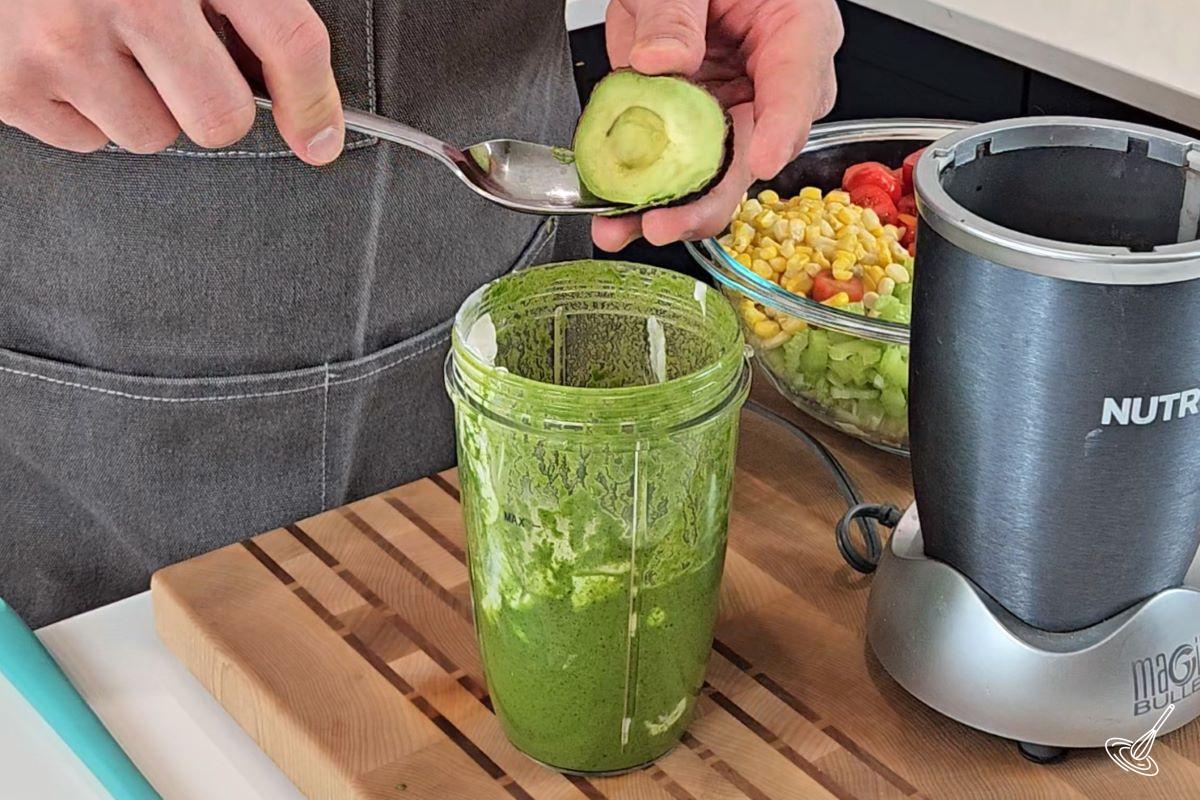 Someone adding an avocado to the jar of a blender. 