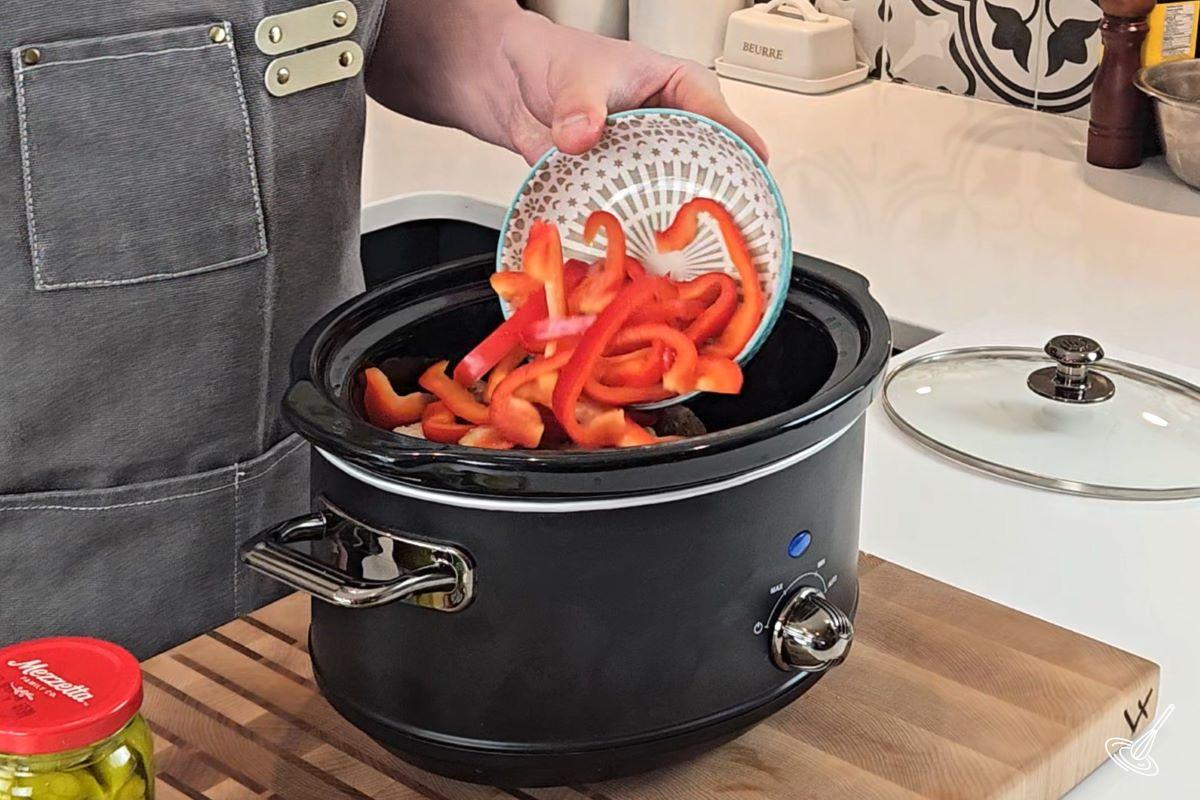 Someone adding sliced bell peppers to a slow cooker.