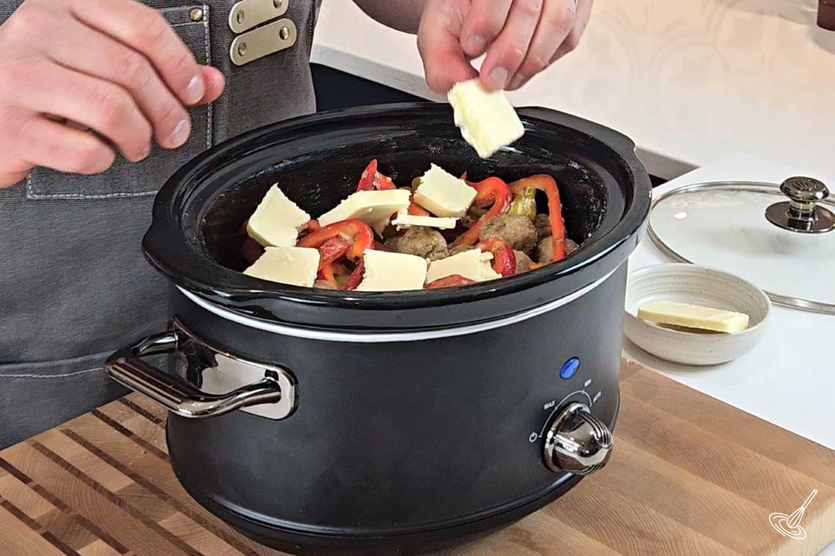 Someone placing pieces of butter over Mississippi meatballs in a slow cooker.